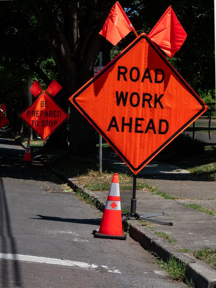 Orange road work ahead sign and cone on city street in Vancouver, WA, under sunny conditions.